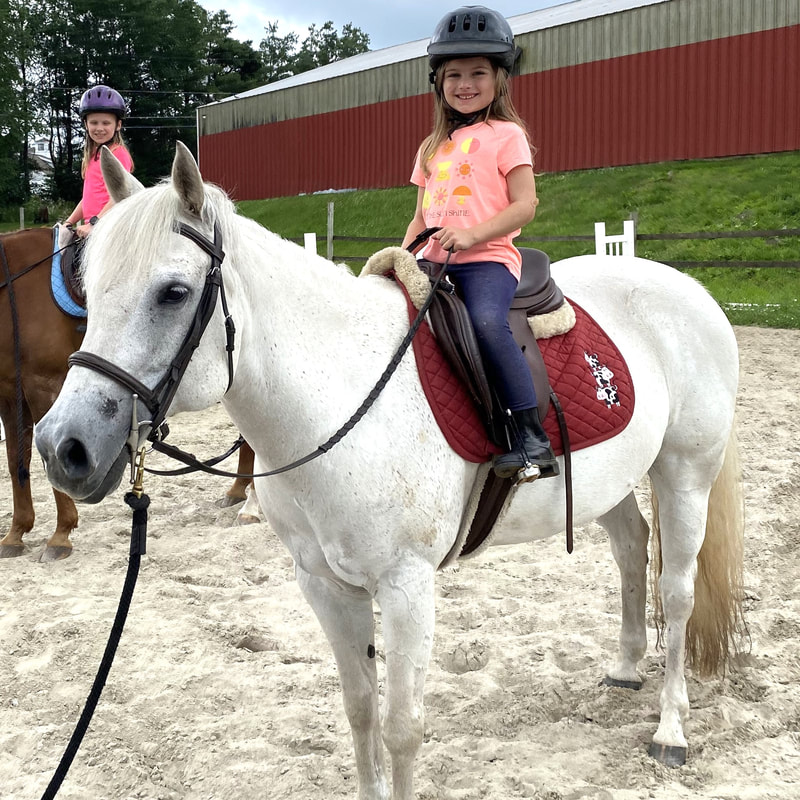 young girl smiling on a gray pony in an outdoor riding ring